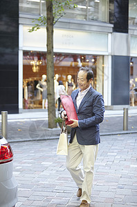 在街上拿着手提袋准备开后备箱的年长男性图片