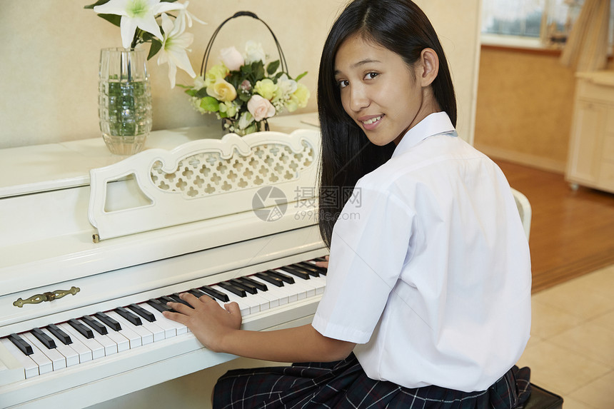 在客厅转头微笑的弹钢琴的女学生图片