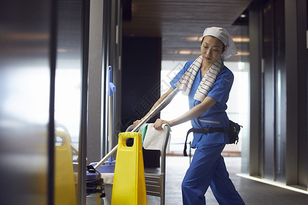 电梯边推着工具的女保洁员图片