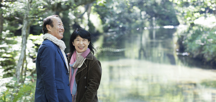 60几岁透过树叶的阳光驯养一对夫妇享受散步图片