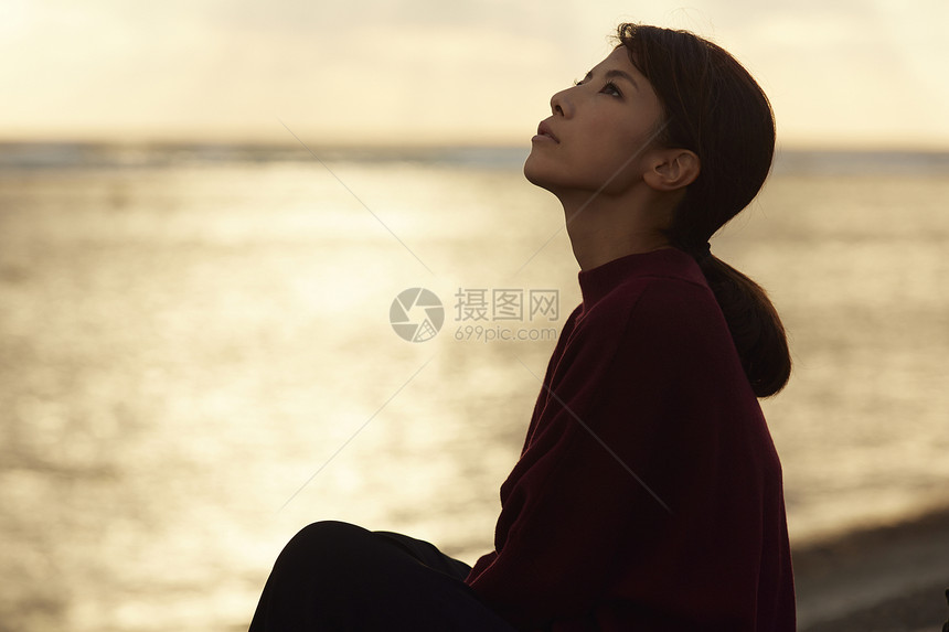 黄昏夕阳下年轻女人坐在海边图片