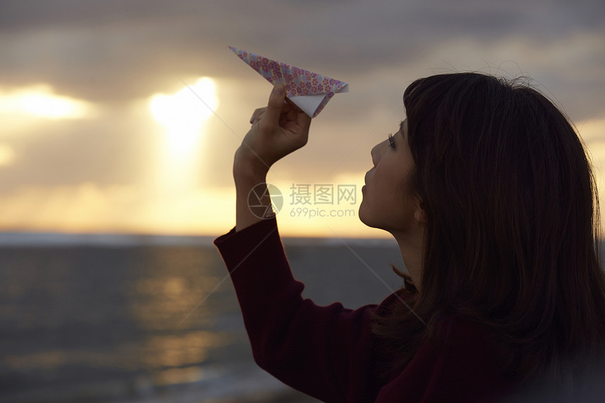 女人在夕阳下手拿纸飞机图片