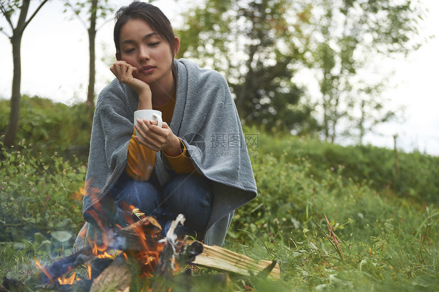 在篝火旁喝水的年轻女人图片