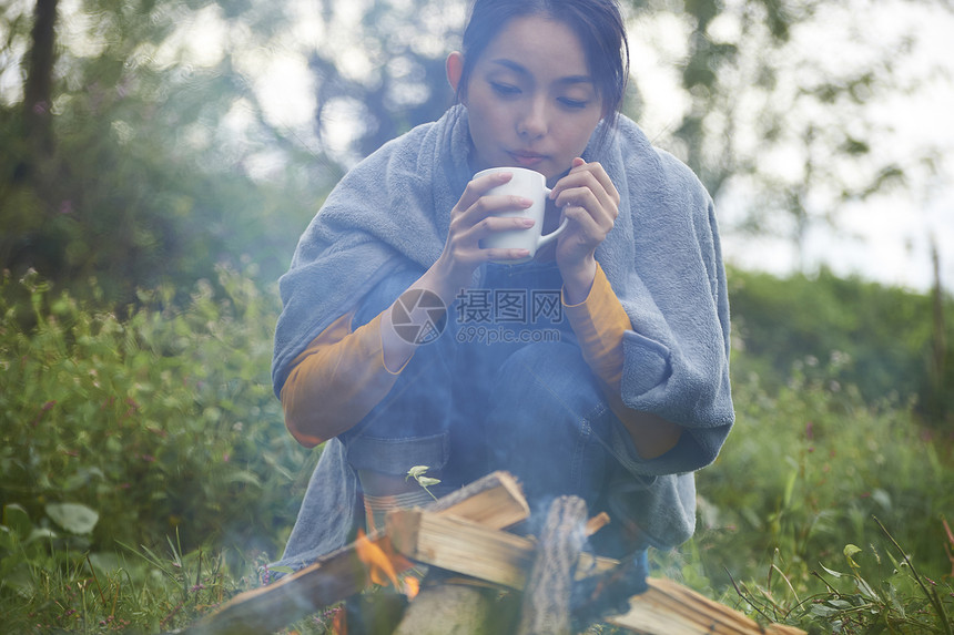 露营时蹲在篝火旁喝咖啡取暖的女性图片