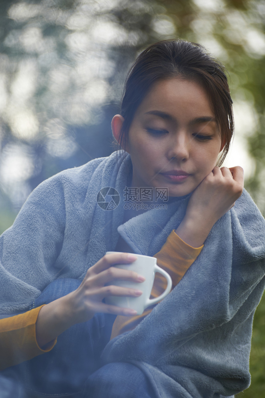 露营时蹲在篝火旁喝咖啡取暖的女性图片