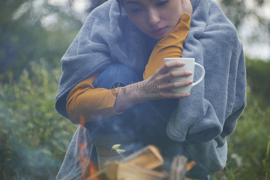 露营时蹲在篝火旁喝咖啡取暖的女性图片