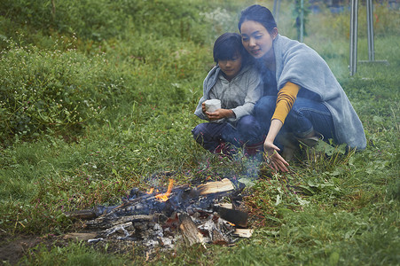 露营时蹲在篝火旁喝咖啡取暖的母子二人图片