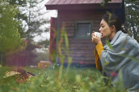 露营时蹲在篝火旁喝咖啡的女性图片