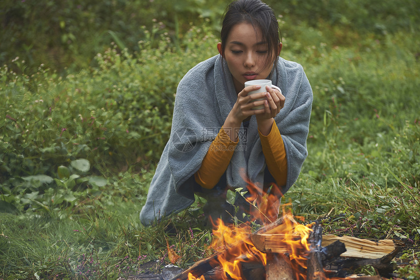 蹲在篝火旁取暖喝咖啡的女人图片