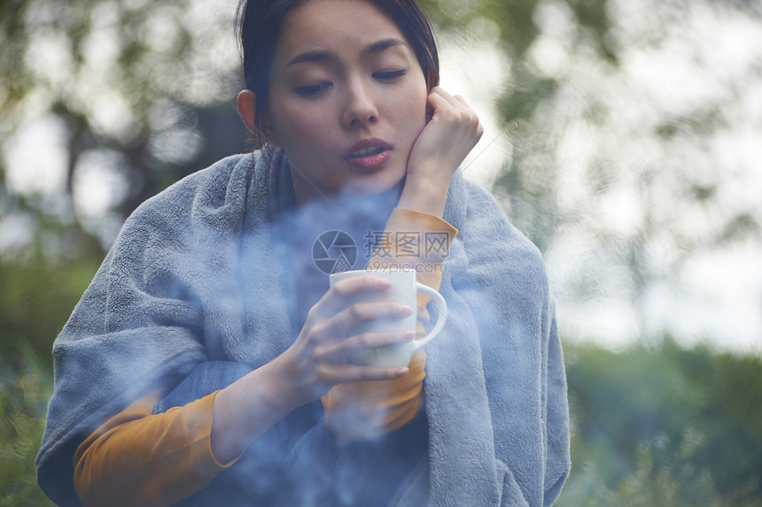蹲在篝火旁取暖喝咖啡的女人图片