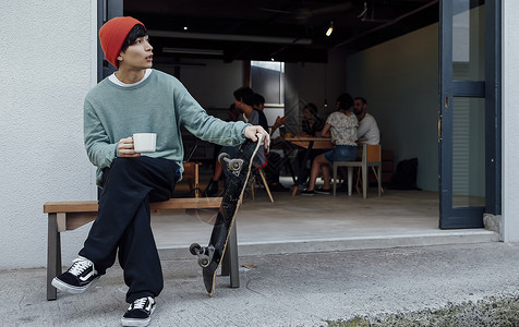 民宿门口拿着滑板喝咖啡的男青年图片