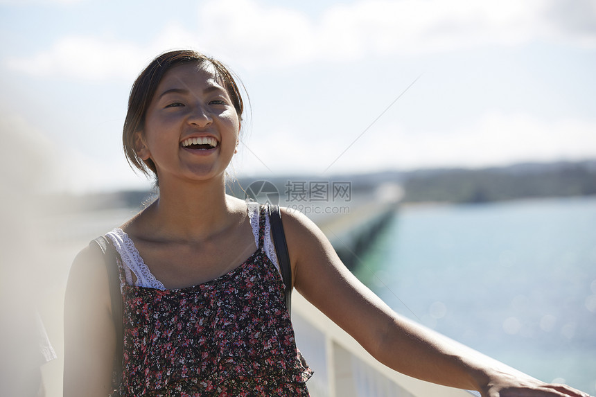 旅途中带着草帽的女性走在海面大桥上大笑图片