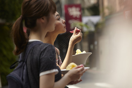 两个女游客在街上拿着刨冰边走边吃高清图片