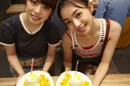 两个女游客坐在放着刨冰的桌边对镜微笑高清图片