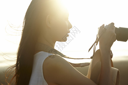 日落时女人站在湿地拿着相机的剪影图片