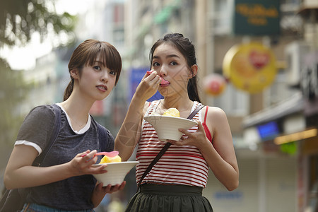 两个女游客在街上拿着刨冰边走边吃图片