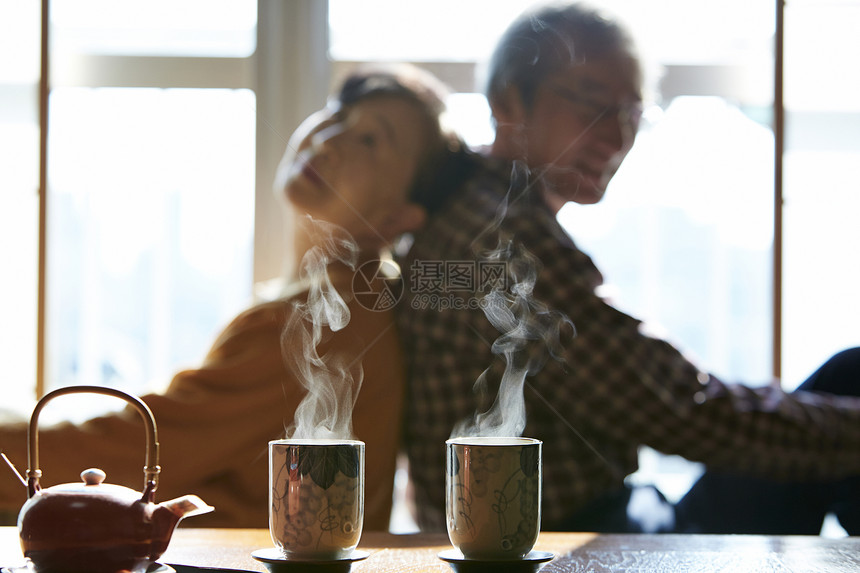 起居室茶桌旁背靠背坐着的老年夫妻图片