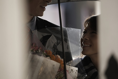 女孩和打着伞拿着花的男友微笑对视图片