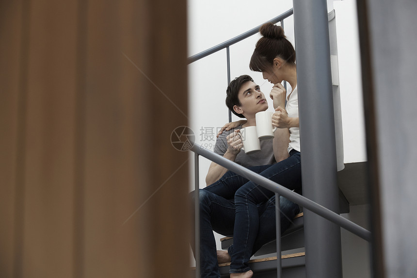 端着杯子的情侣坐在楼梯上说笑图片