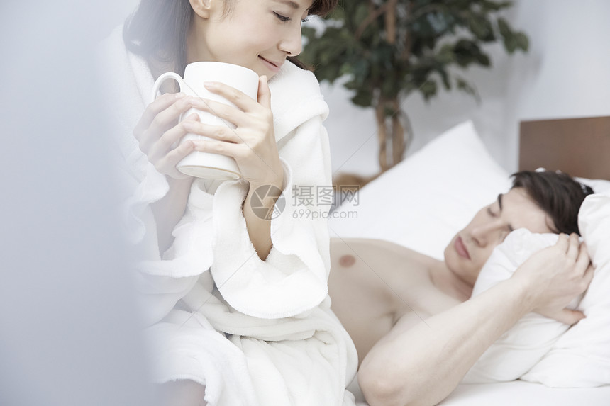 女人端着杯子看床上睡觉的男人图片