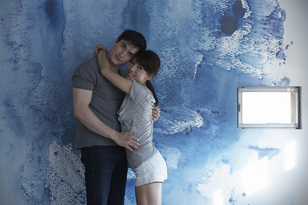 蓝色墙壁前看着镜头的情侣图片