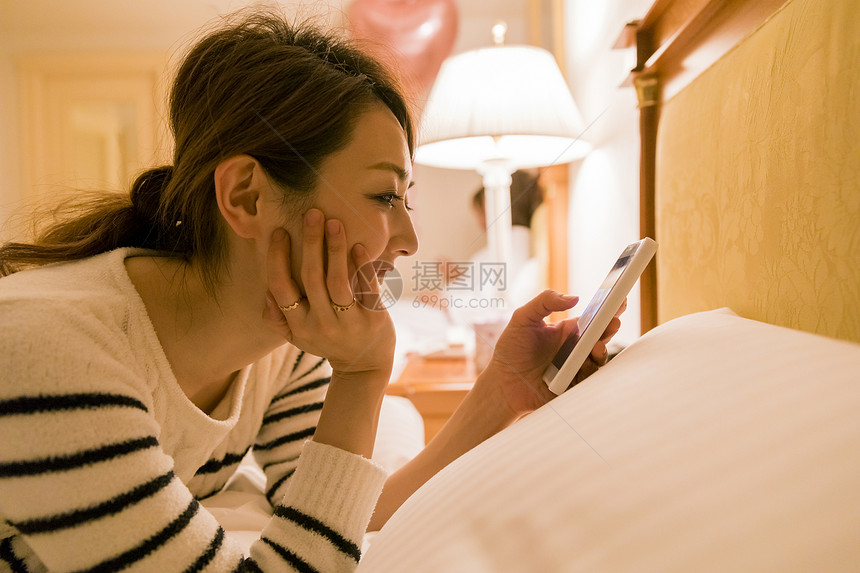 女人穿着睡衣趴在床上玩手机图片