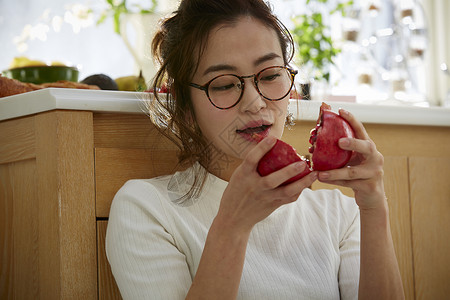 在窗边料理台蹲下看切开的石榴的女人背景图片