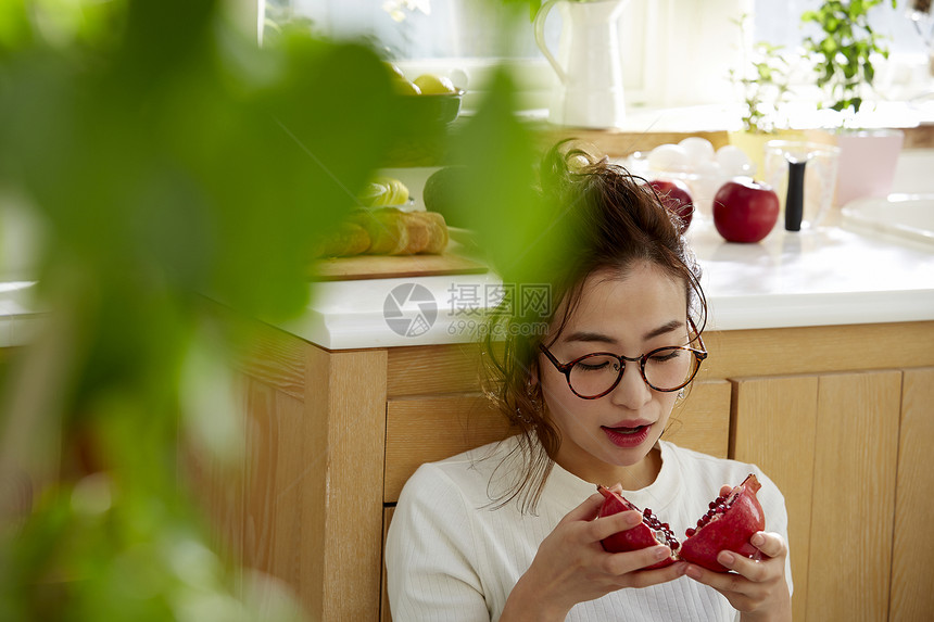 在窗边料理台蹲下看切开的石榴的女人图片