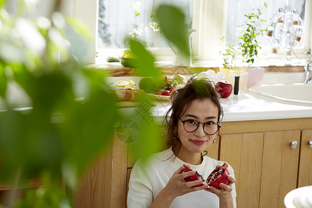 在窗边料理台蹲下看切开的石榴的女人背景图片