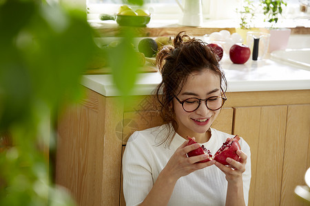 在窗边料理台蹲下看切开的石榴的女人背景图片