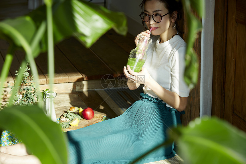 坐在木地板上晒着太阳喝奶昔的女人图片