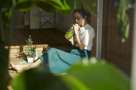 坐在木地板上晒着太阳喝奶昔的女人图片