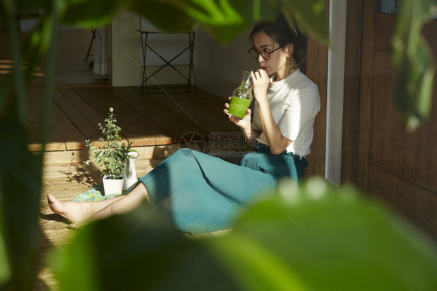 坐在木地板上晒着太阳喝奶昔的女人图片