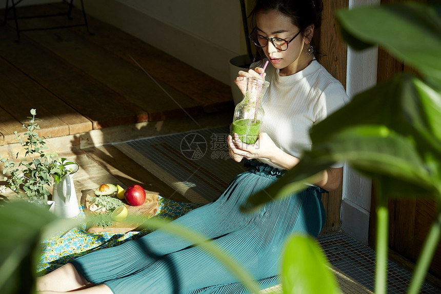 坐在木地板上晒着太阳喝奶昔的女人图片