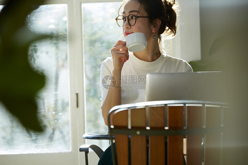 女人坐在窗边的桌上喝咖啡工作图片