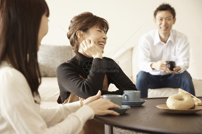 男人坐在沙发上和两个坐在桌边的女人喝茶聊天图片