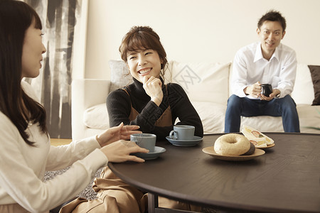 男人坐在沙发上和两个坐在桌边的女人喝茶聊天图片