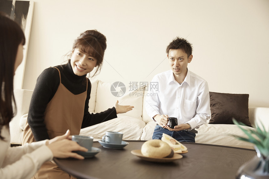 男人坐在沙发上和两个坐在桌边的女人喝茶聊天图片