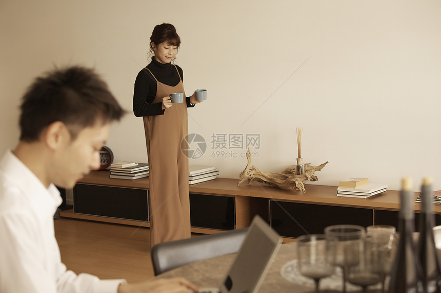 男人坐着用电脑工作女人端着咖啡站着图片