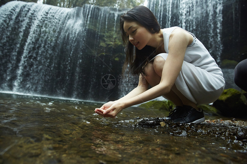 站在小溪边享受瀑布的女人用手捧水图片