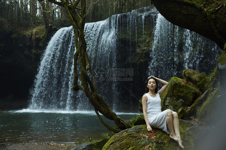 坐在小溪边享受瀑布的女人抬头看图片