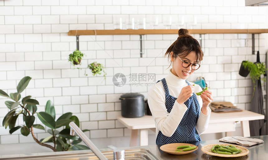 戴眼镜的年轻女孩穿着围裙在厨房烹饪蔬菜图片