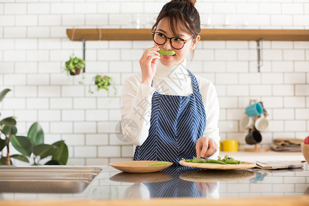 戴眼镜的年轻女孩穿着围裙在厨房烹饪蔬菜图片