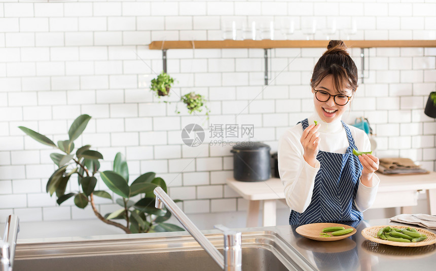 戴眼镜的年轻女孩穿着围裙在厨房烹饪蔬菜图片