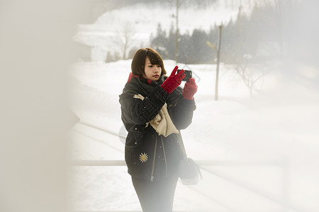冬天女孩在雪景中用手机拍摄图片