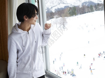 在窗边看雪景的男性图片