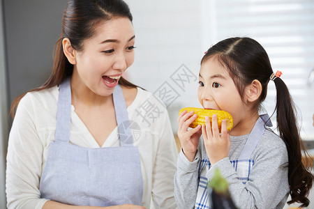 妈妈看着女儿吃玉米背景图片