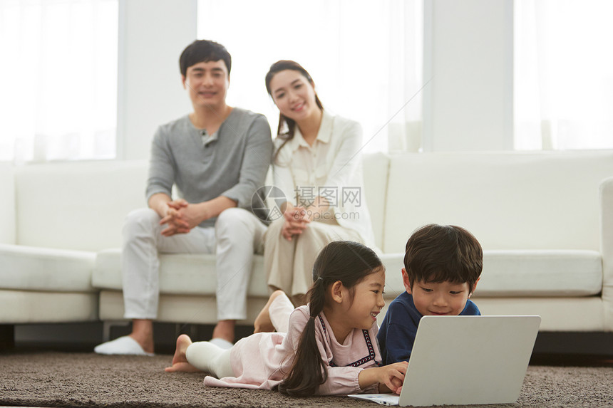 父母看着趴在地上玩电脑的孩子们图片