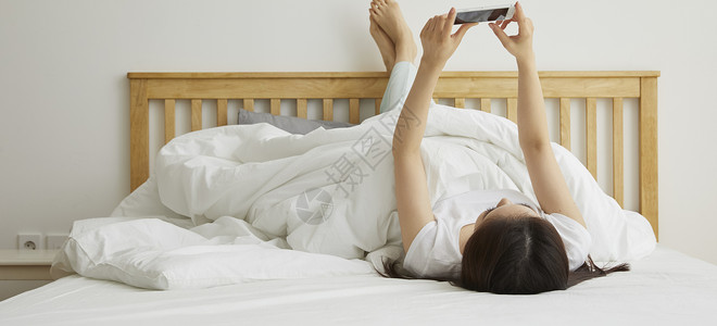 躺在床上玩手机的年轻女性图片