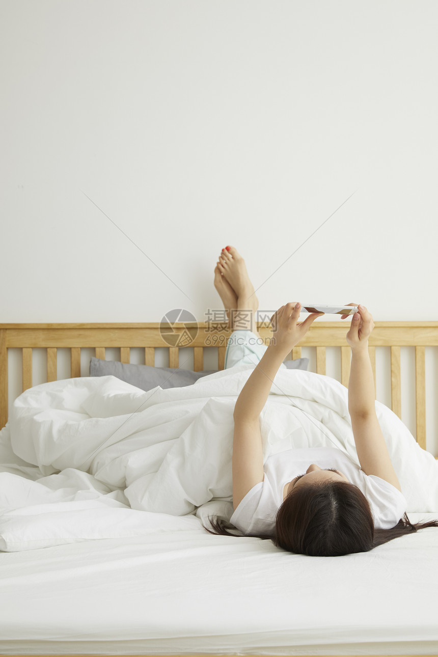躺在床上玩手机的居家女性日常生活图片